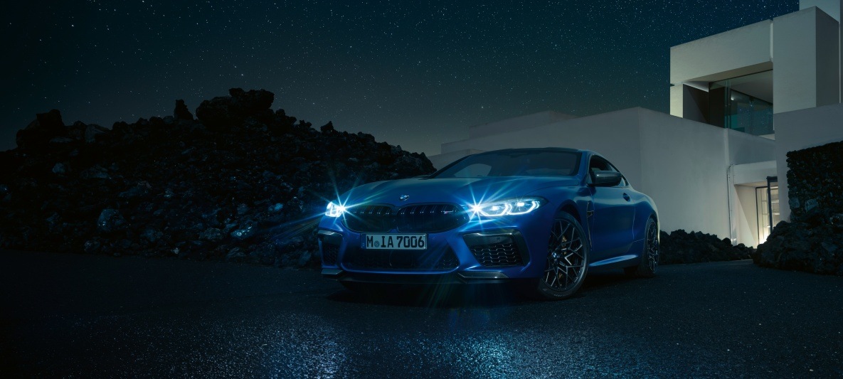 BMW M8 Competition Coupé Ein blaues BMW M8 Competition Coupé steht vor einem modernen Wohnhaus