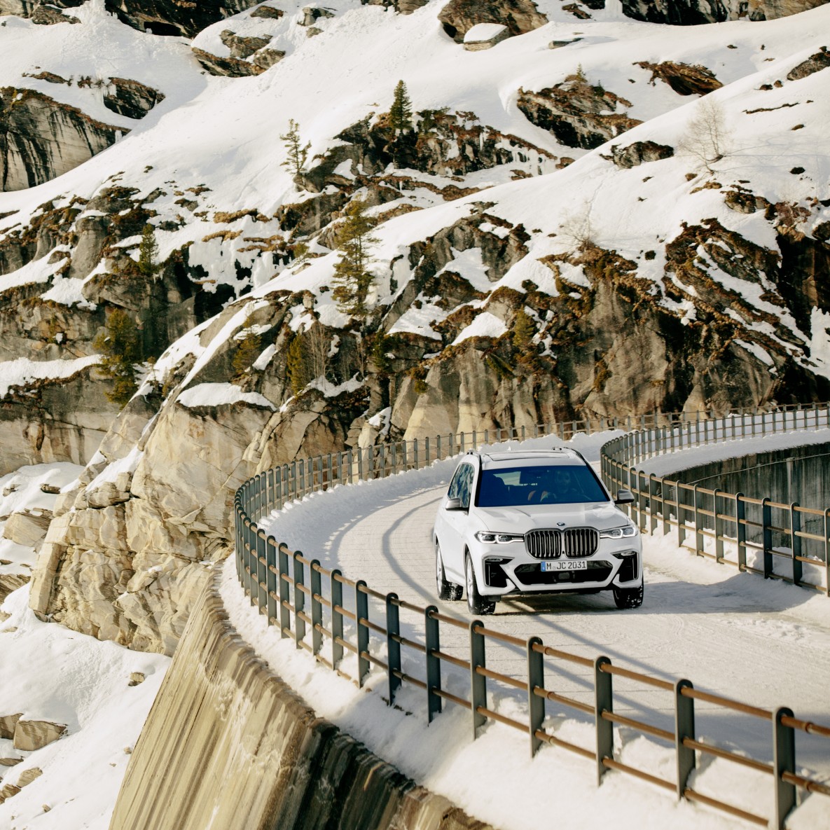 A white BMW X7 M50d drives on a snowy bridge in the Swiss Alps