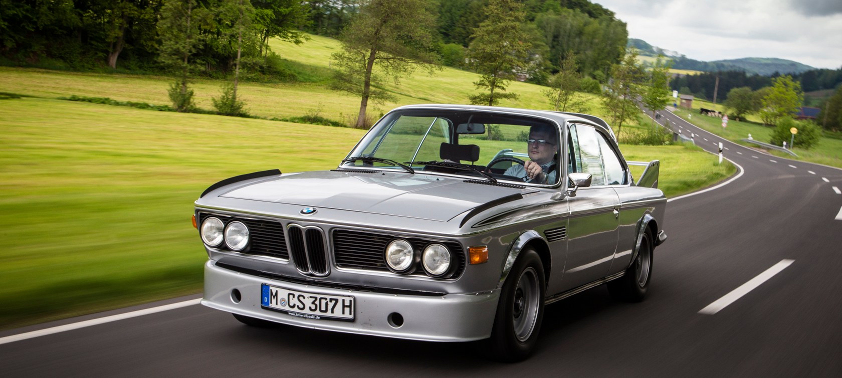 Front view of a BMW 3.0 CSL driving on a country road