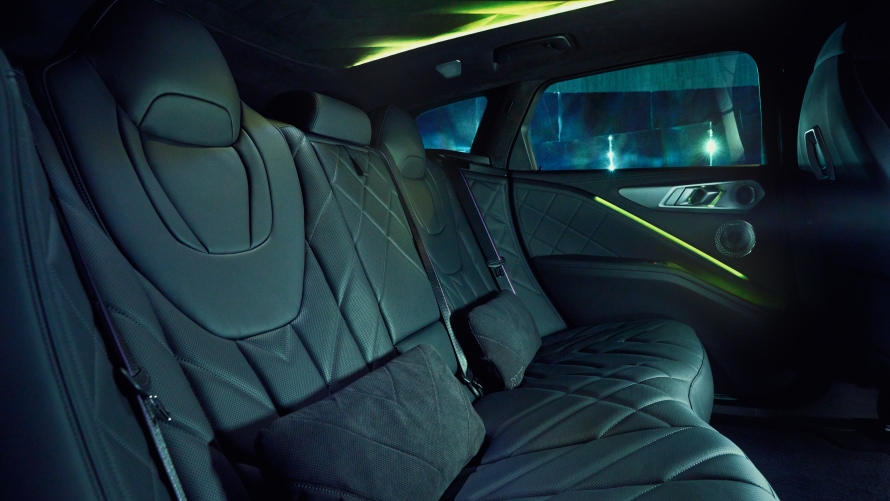 M LOUNGE. A generous feeling of space, high-quality materials and extravagant design transform the rear of the BMW XM 50e into an exclusive M Lounge. The one-piece seating area and details such as the diamond-shaped structures in the headrests and stitching pattern convey comfort and luxury. Together with the sculptural, indirectly illuminated headliner, dark windows and comfort cushions, they create a novel feeling of space.