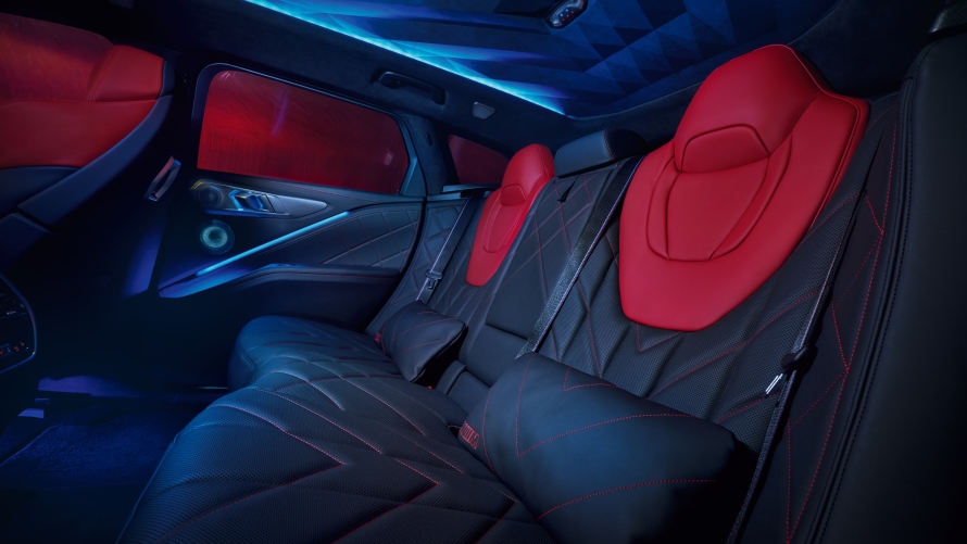 M LOUNGE. A generous feeling of space, high-quality materials and extravagant design transform the rear of the BMW XM Label Red into an exclusive M Lounge. Optionally heated backrests that extend well into the sides of the cabin and cushions in Merino leather with red contrast stitching and an "XM" badge offer passengers luxurious levels of comfort. Red is used to bring an extra sense of exclusivity to the diamond-shaped upper sections of the backrests and the integrated head restraints of the seats. Together with the sculptural, indirectly illuminated headliner, dark windows and comfort cushions, they create a novel feeling of space.