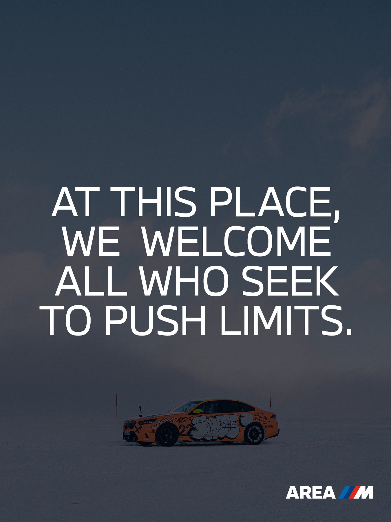 Ein Bild mit einem orangefarbenen BMW Sportwagen auf einer verschneiten Landschaft unter dunklem Himmel. In weißer Schrift steht: 'AT THIS PLACE, WE WELCOME ALL WHO SEEK TO PUSH LIMITS.' Das BMW M Logo erscheint in der unteren rechten Ecke mit dem Text 'AREA M'.