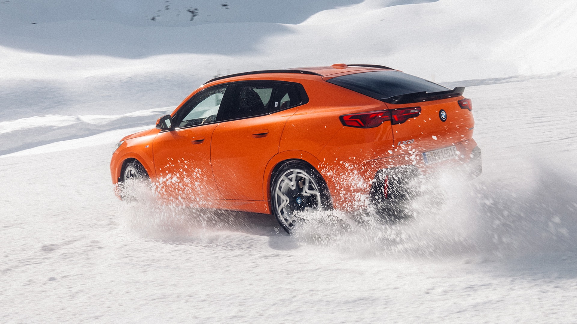 Ein orangefarbener BMW SUV fährt durch tiefen Schnee und erzeugt dabei eine Schneewolke, während er sich durch eine weiße Winterlandschaft bewegt.