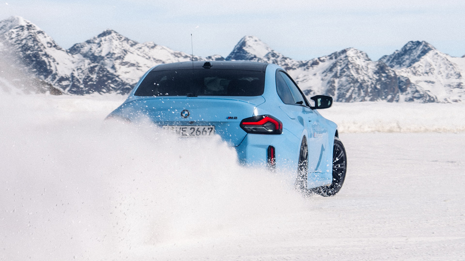 Drifting BMW M blue in rear view in snow in front of snow-covered mountain range