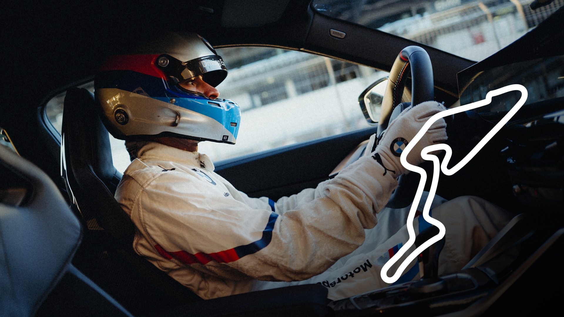 Ein Rennfahrer in einem weißen Rennanzug mit rot-weiß-blauem Helm sitzt in einem BMW Sportwagen. Der Fahrer umgreift mit Handschuhen das Lenkrad. Im Hintergrund ist eine Rennstrecke zu sehen, und auf der rechten Seite des Bildes ist ein weißer Streckenumriss erkennbar.