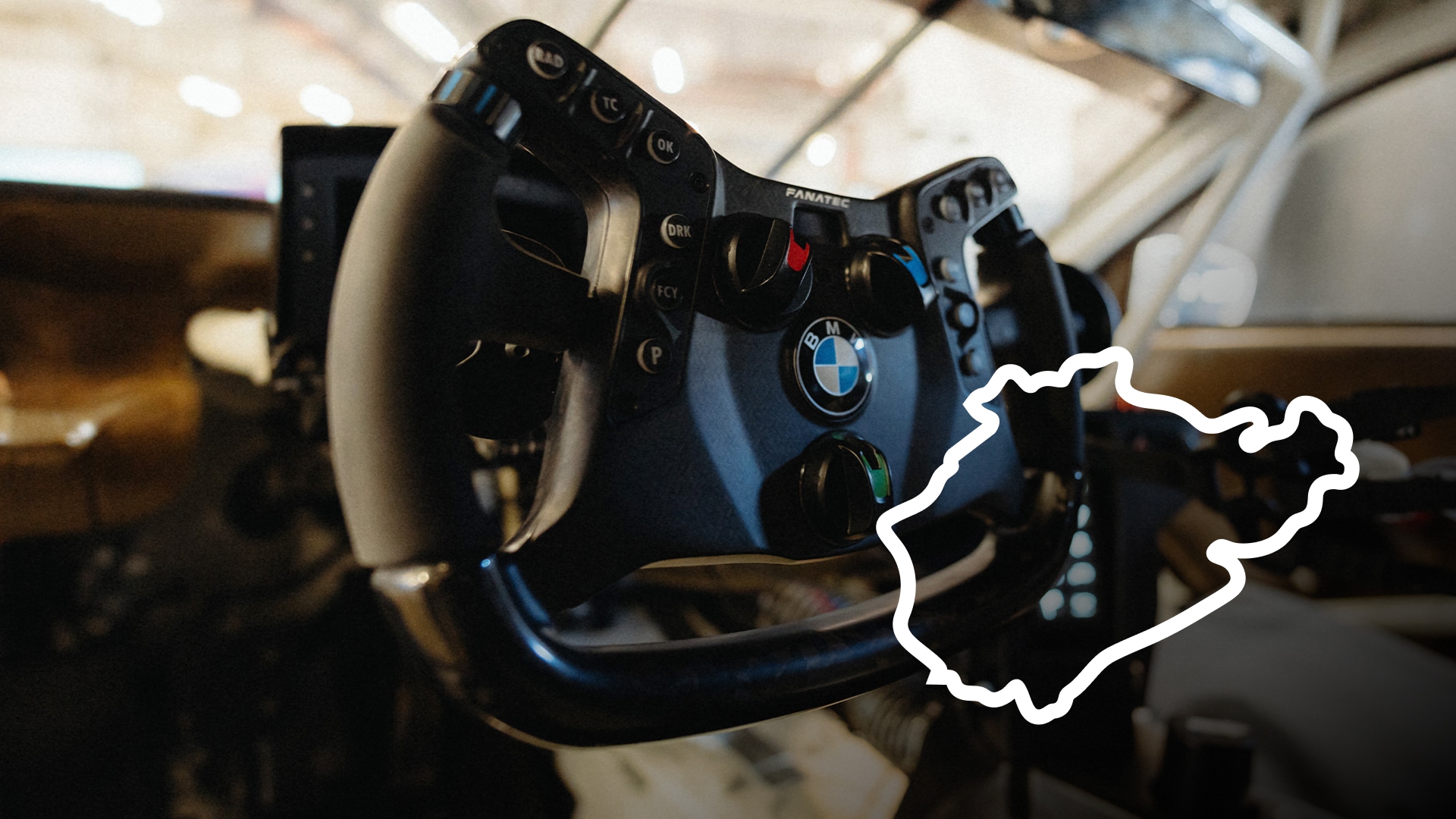 Ein Fanatec-Rennsimulatoren-Lenkrad mit BMW-Branding. Das schwarze Lenkrad verfügt über mehrere Tasten und Bedienelemente. Im Hintergrund ist eine weiße Umrisszeichnung der Nürburgring-Rennstrecke zu sehen.