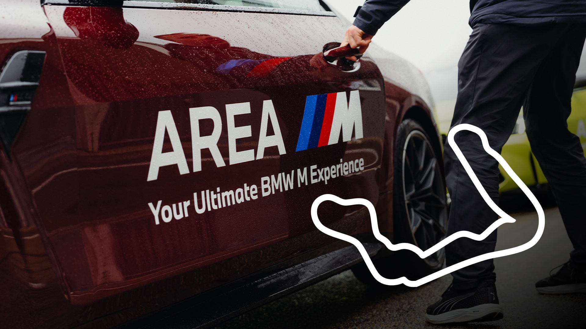 Ein burgunderroter BMW mit der Aufschrift "AREA M" und "Your Ultimate BMW M Experience" auf der Tür. Eine Person in dunkler Kleidung öffnet die Autotür. Im Vordergrund des Bildes ist ein weißer Umriss einer Rennstrecke zu sehen.