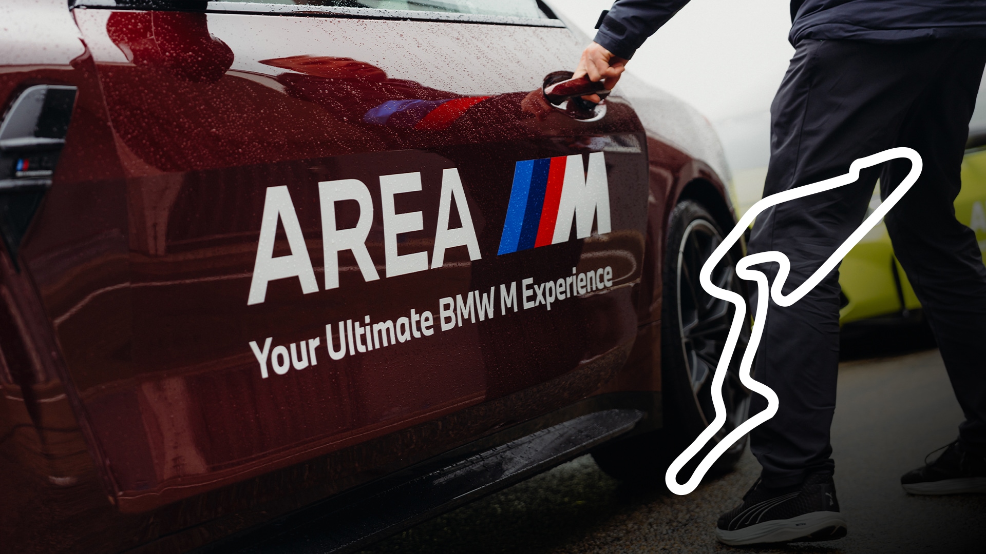 Eine Nahaufnahme eines dunkelroten BMW mit "AREA M"-Branding und dem Text "Your Ultimate BMW M Experience" auf der Tür. Eine Person in dunkler Kleidung öffnet die Autotür. Ein weißer Umriss einer Rennstrecke ist auf der rechten Seite des Bildes zu sehen.