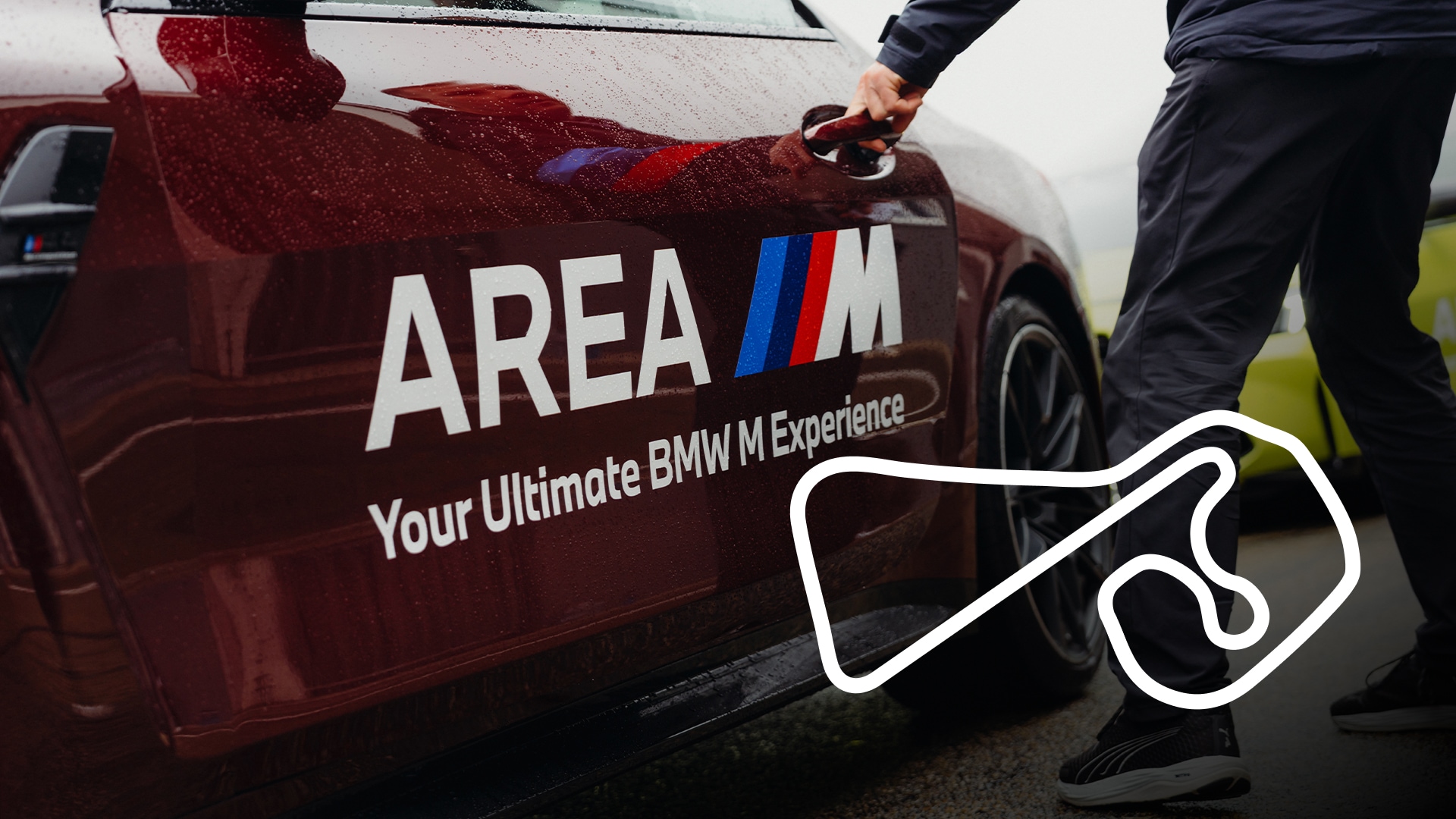 Ein dunkelrotes BMW-Fahrzeug mit "AREA M"-Branding und dem Text "Your Ultimate BMW M Experience" auf der Tür. Eine Person in dunkler Kleidung öffnet die Autotür. Im unteren rechten Bildbereich ist der weiße Umriss einer Rennstrecke zu sehen.