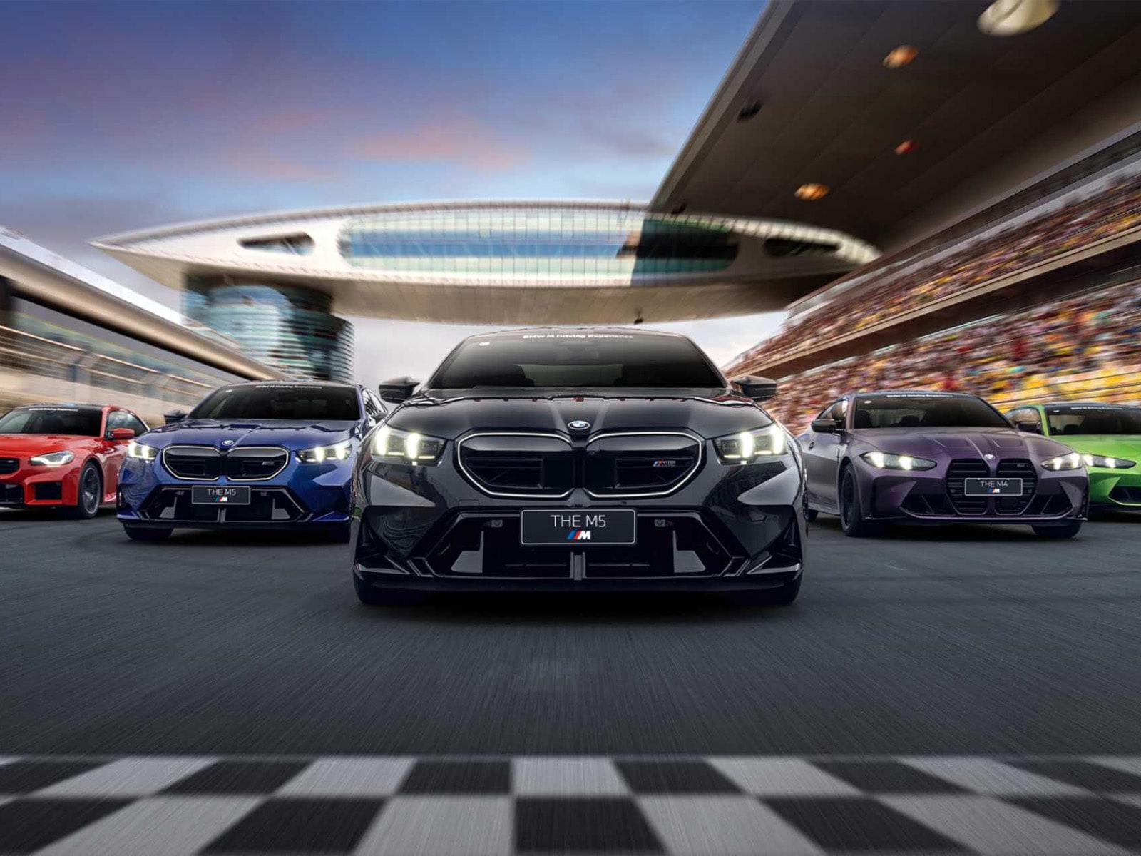 Eine Reihe von BMW Fahrzeugen auf einer Rennstrecke mit einer schwarz-weiß karierten Ziellinie im Vordergrund. Der zentrale schwarze M5 wird von blauen, roten, violetten und grünen Modellen flankiert. Im Hintergrund sind eine moderne architektonische Struktur und vollbesetzte Tribünen zu sehen.