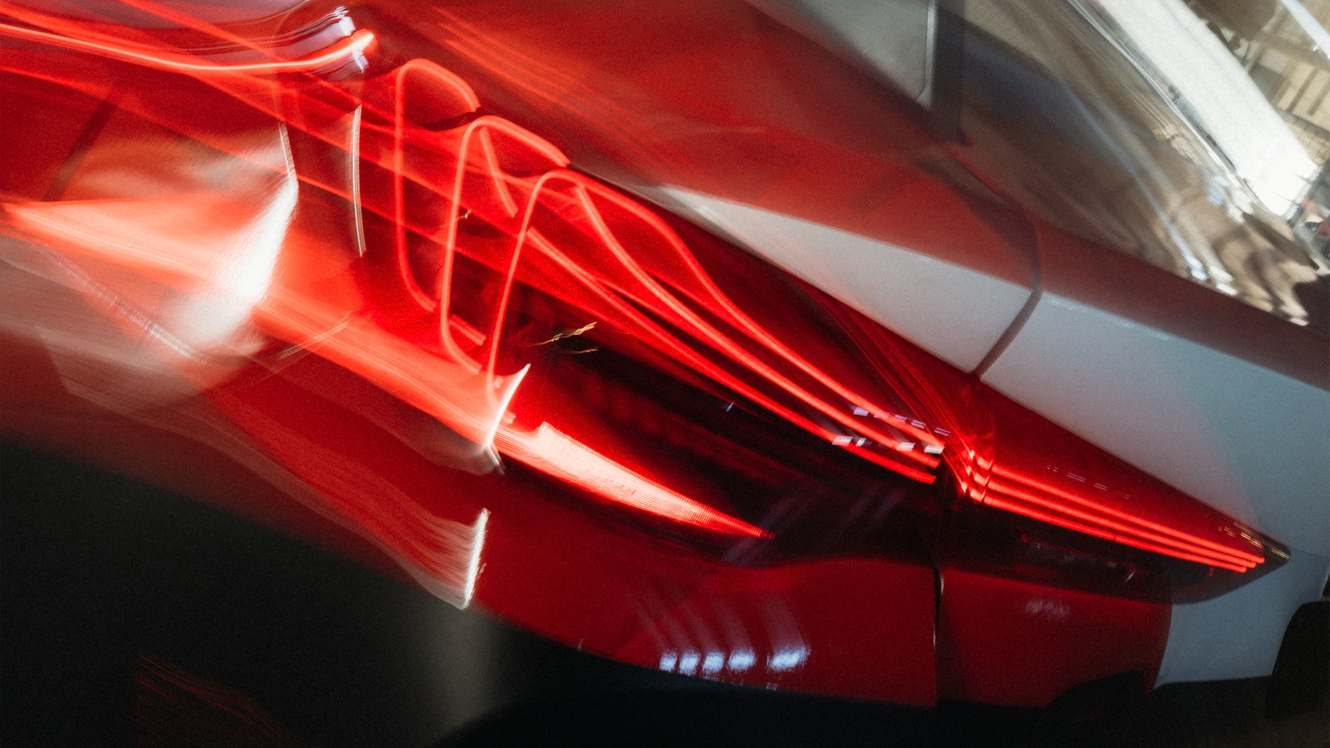 Eine verwischte Bewegungsaufnahme eines modernen Autoscheinwerfers mit hellroten LED-Lichtstreifen, die dynamische Lichtspuren an einer hellen Fahrzeugkarosserie erzeugen.