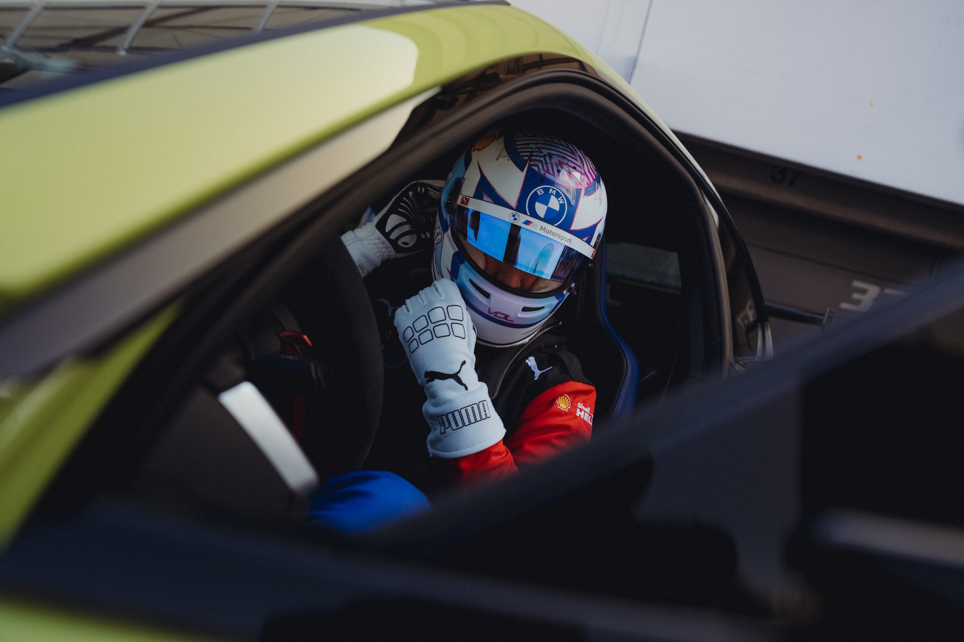 Driver wearing a BMW M Motorsport helmet and racing suit in the cockpit of a lime green BMW