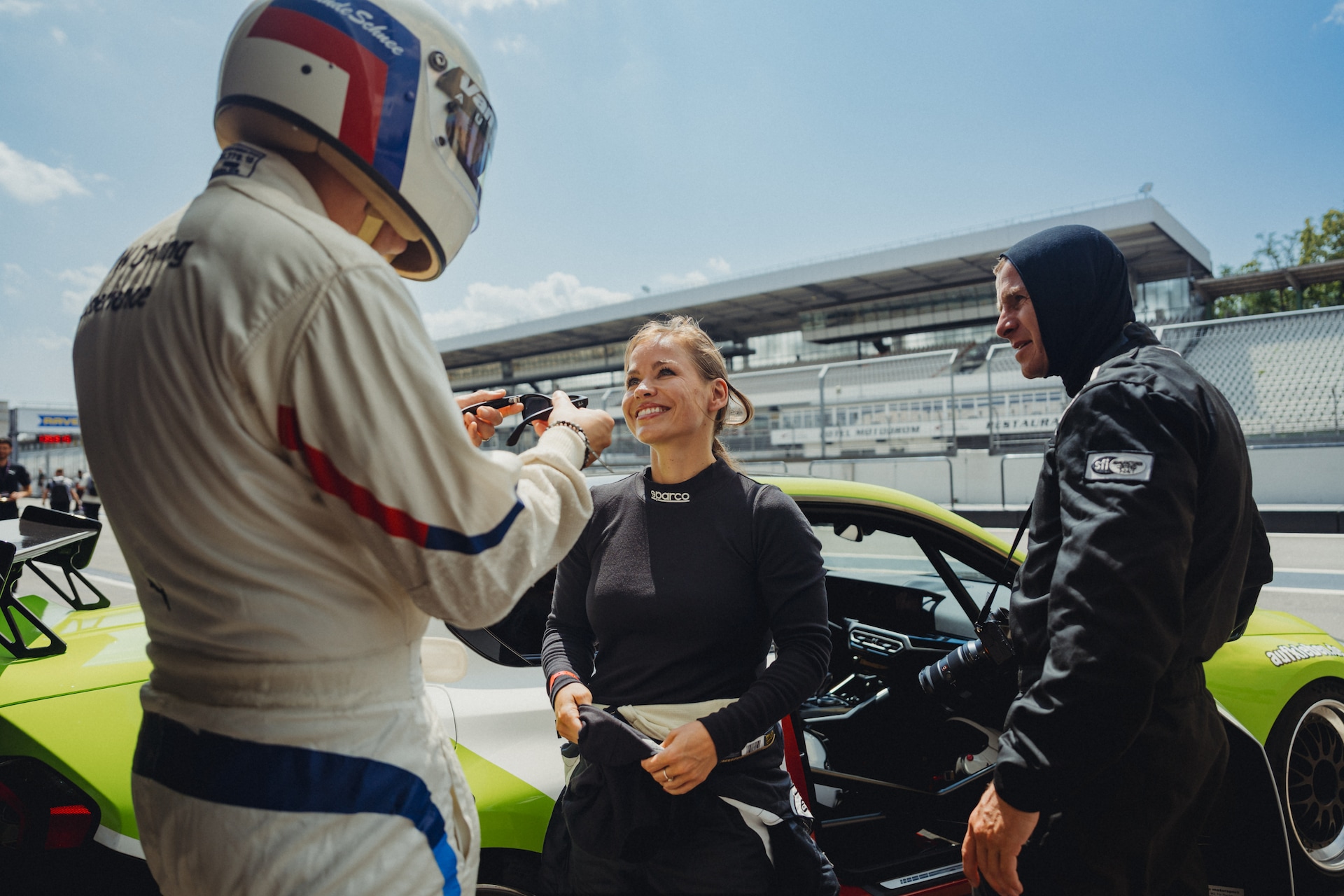 Driver and co-driver in racing suits sharing a moment in front of a lime green BMW in the Hockenheim pit lane, with a camera crew in the background