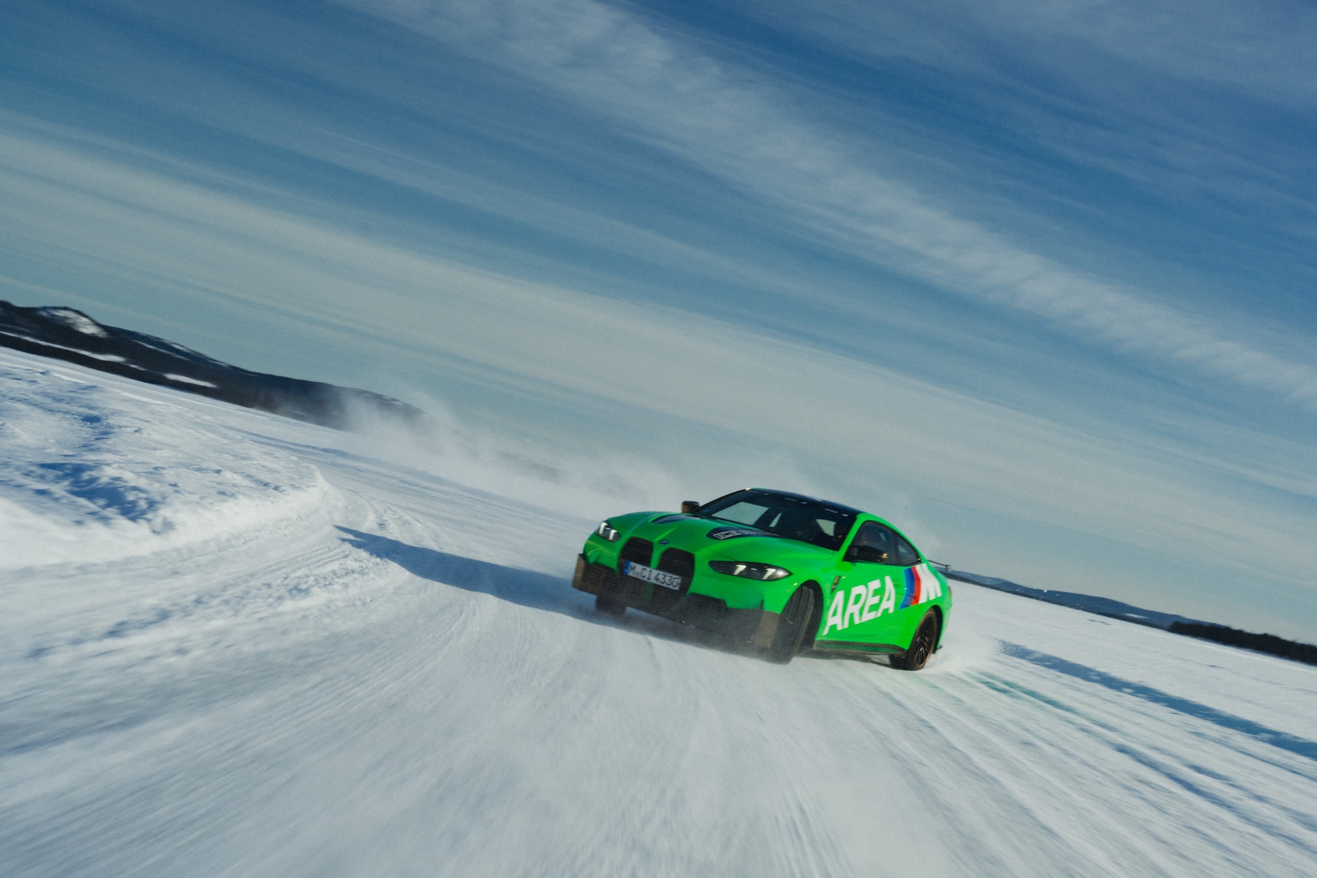 Ein leuchtend grünes Auto mit 'AREA'-Beschriftung fährt über eine verschneite, vereiste Landschaft unter klarem blauem Himmel. Schnee wirbelt um das Fahrzeug auf, während es über das gefrorene Gelände fährt, mit schneebedeckten Hügeln im Hintergrund.