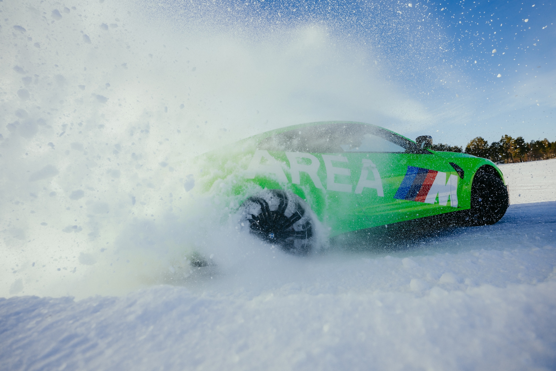 Ein leuchtend grüner Sportwagen beschleunigt über eine verschneite Landschaft und erzeugt eine große Schneewolke. Das Fahrzeug hat einen blauen und roten Streifen an der Seite und wird bei einer Driftfahrt auf einer gefrorenen Oberfläche mit Bäumen im Hintergrund unter klarem blauen Himmel erfasst.