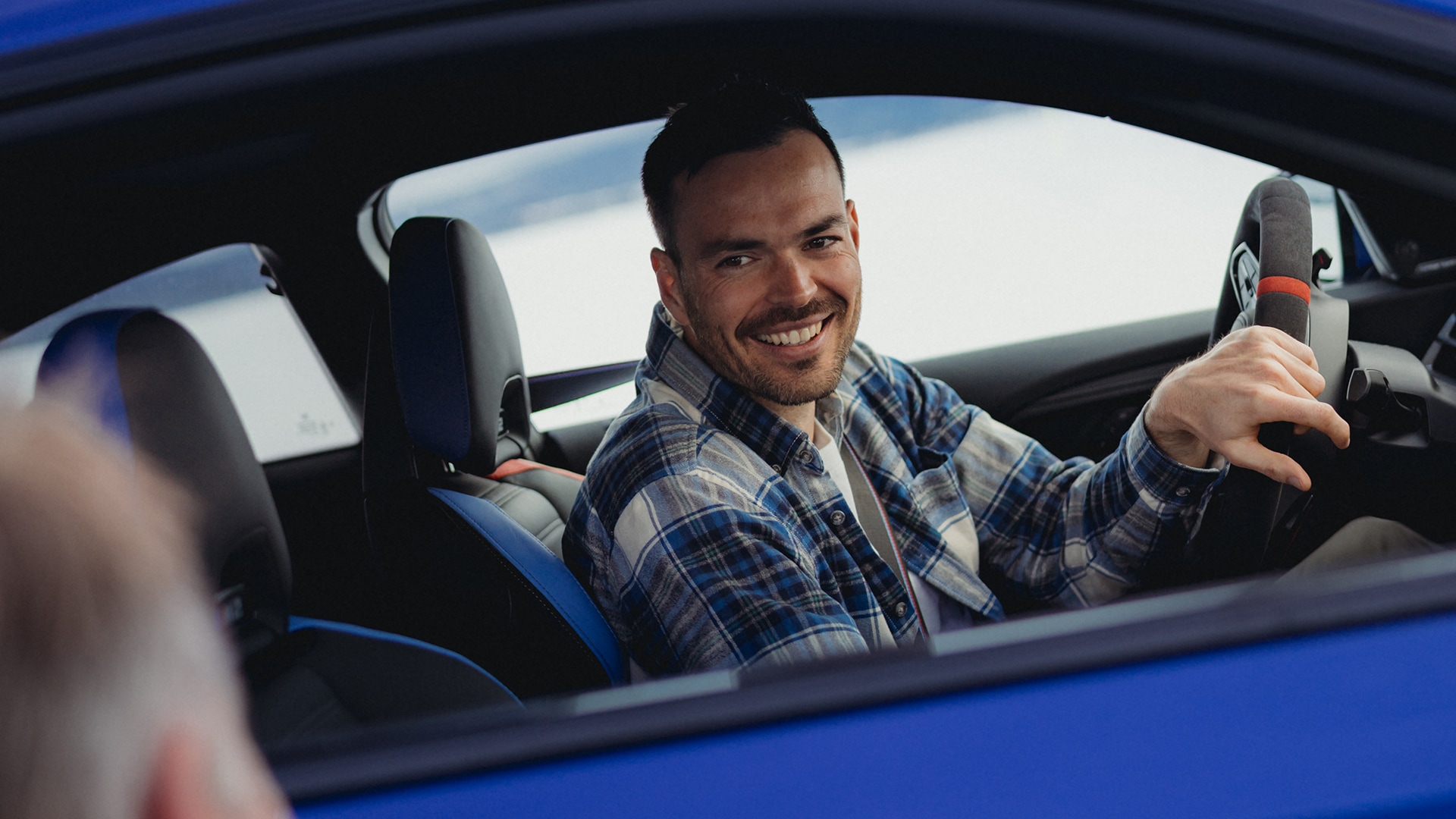 Lächelnder Mann am Steuer eines BMW M blau mit M Sportlenkrad