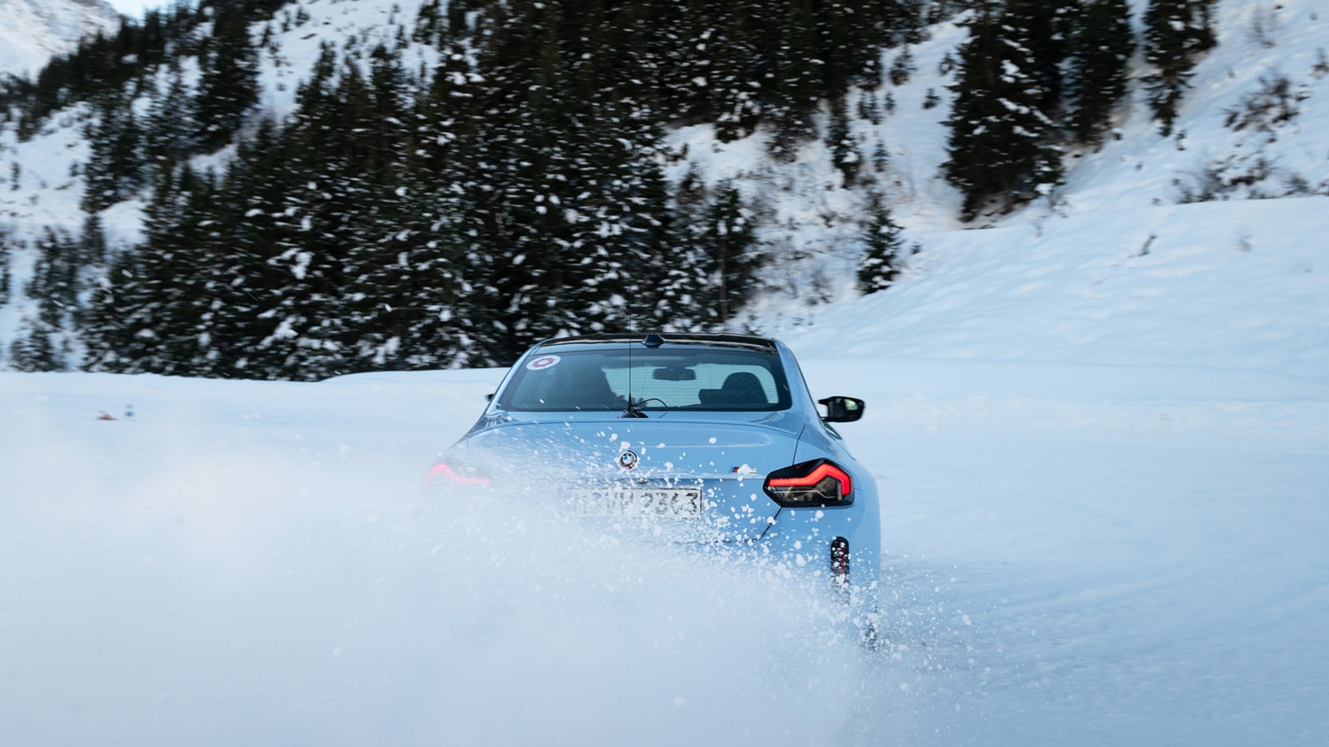 BMW M blau in Heckansicht im Drift im Schnee vor verschneitem Nadelwald am Berghang