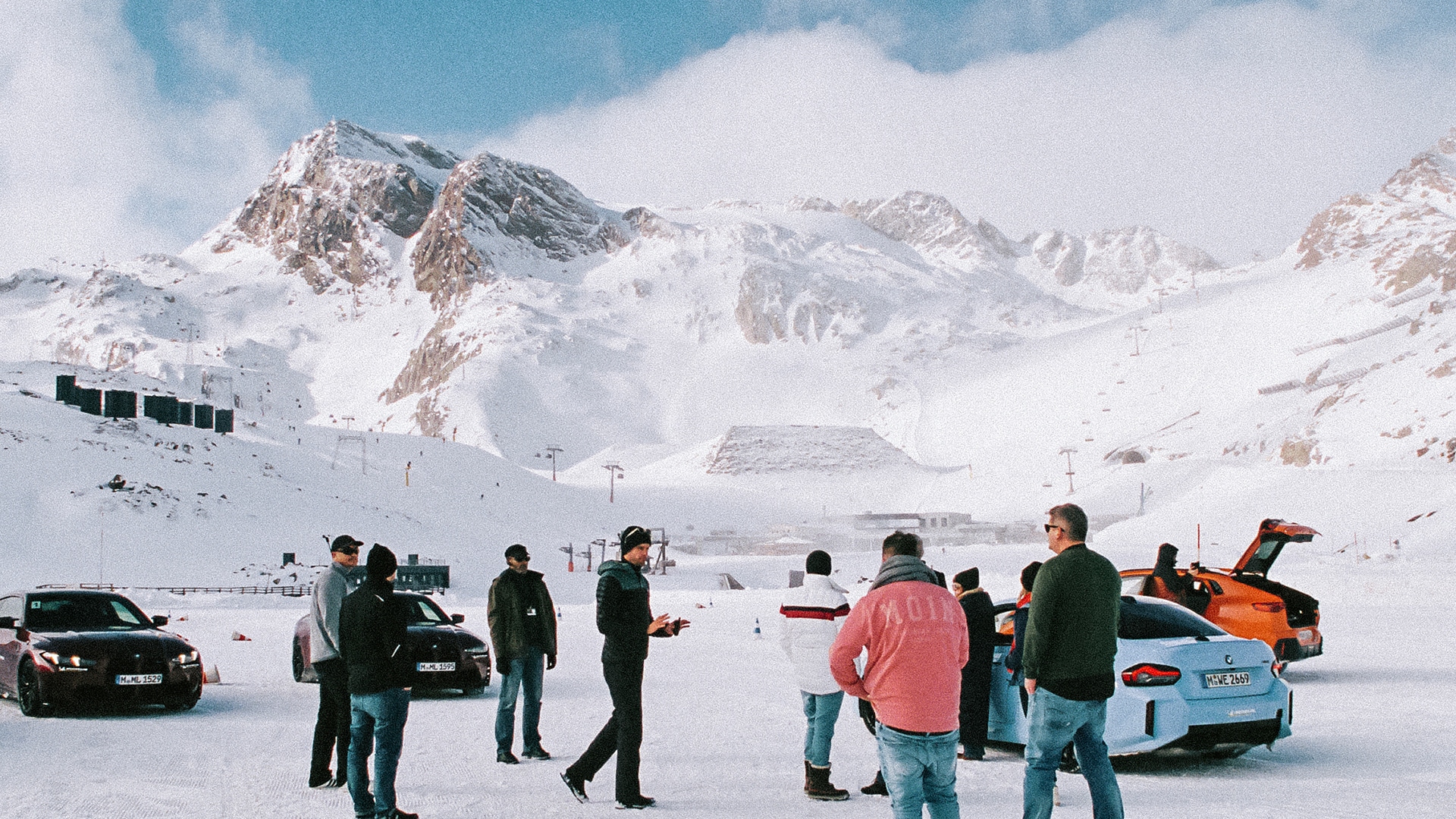 Teilnehmergruppe im Gespräch vor mehreren BMW Fahrzeugen auf Schneepiste, im Hintergrund verschneite Berglandschaft