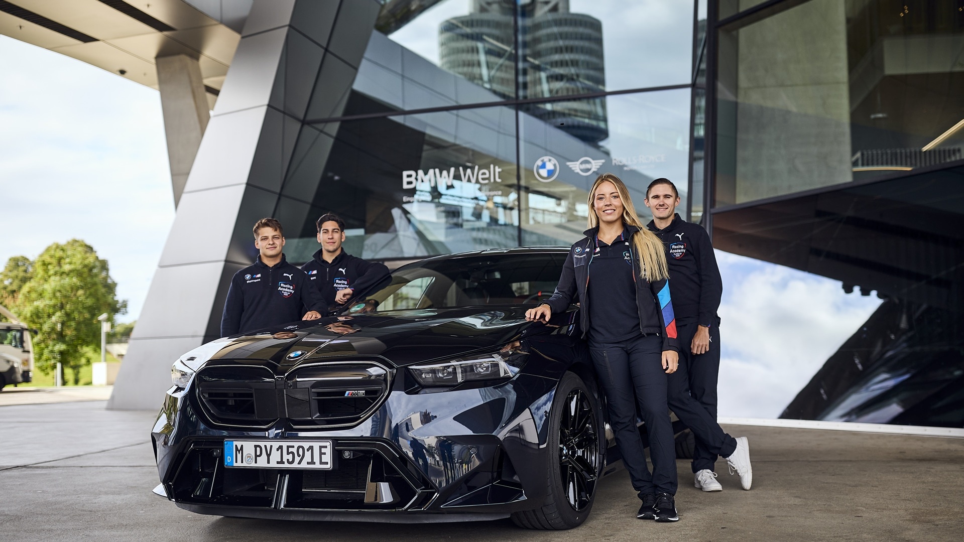 Nils Tröger, Berkay Besler, Nerea Martí und Matt Million posieren zum Gruppenbild mit einem BMW M5.