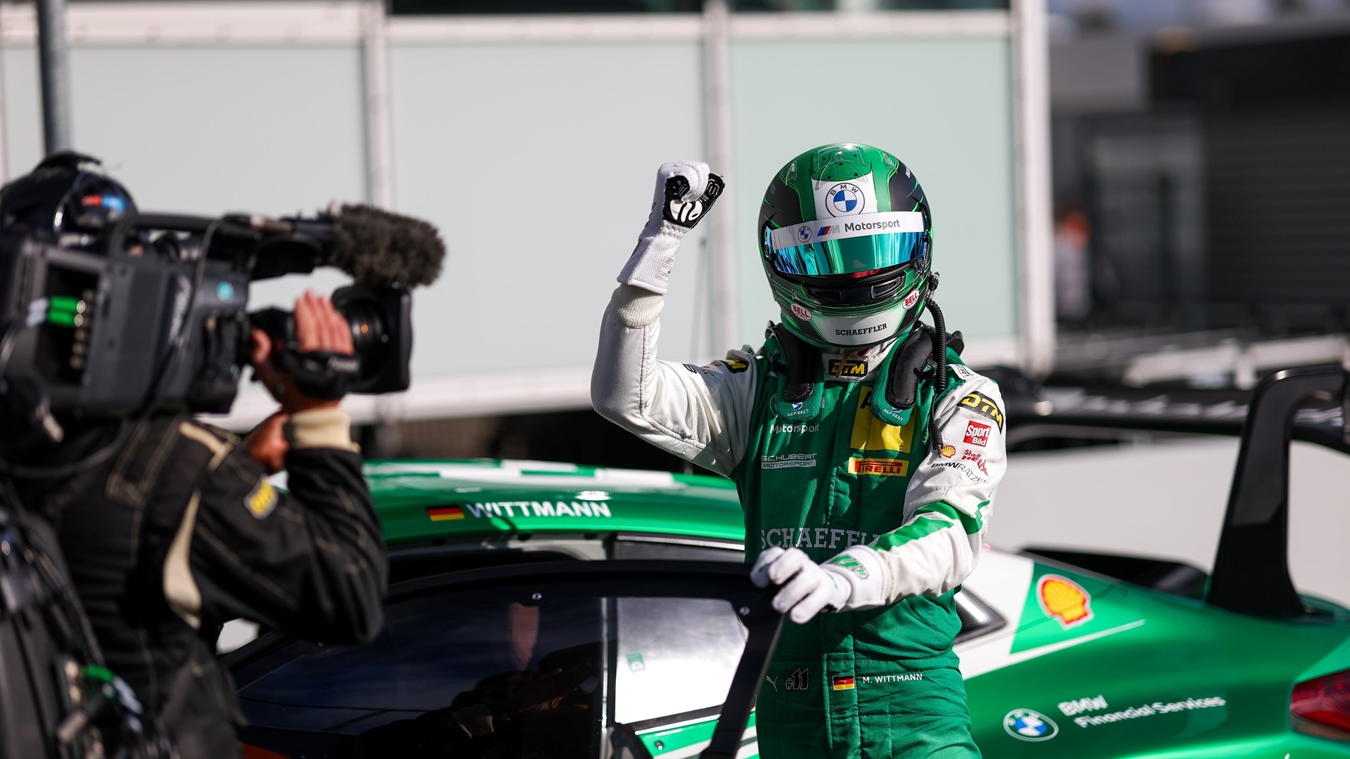 Marco Wittmann stands next to his BMW M4 GT3 EVO, raising his arm in the air in a gesture of triumph.