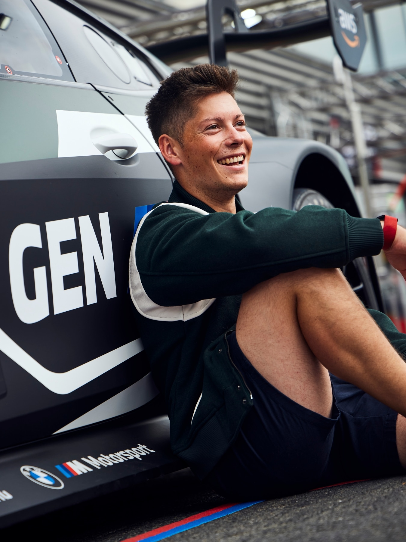 BMW M Werksfahrer Max Hesse sitzt vor dem BMW M4 GT3 EVO von Rowe Racing mit GEN-M-Livery