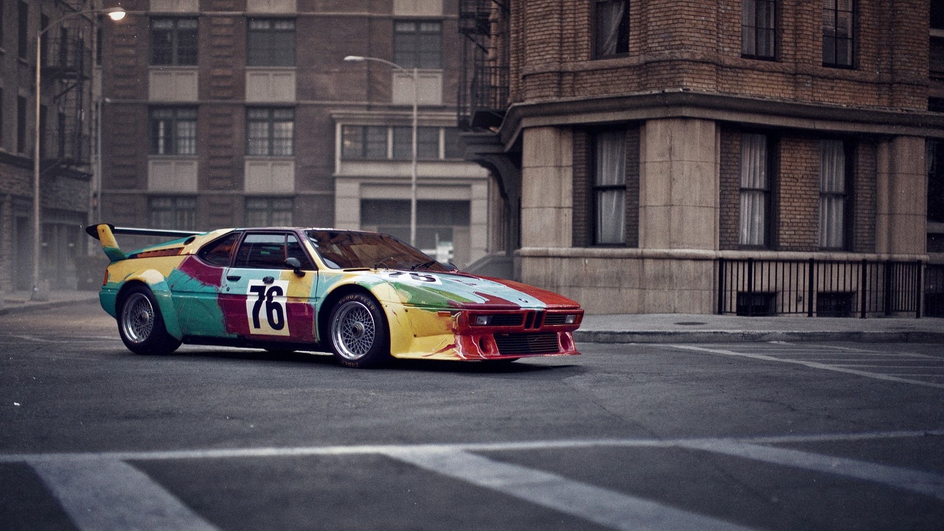 The BMW M1 Art Car by Andy Warhol before the backdrop of a an American inner city street.