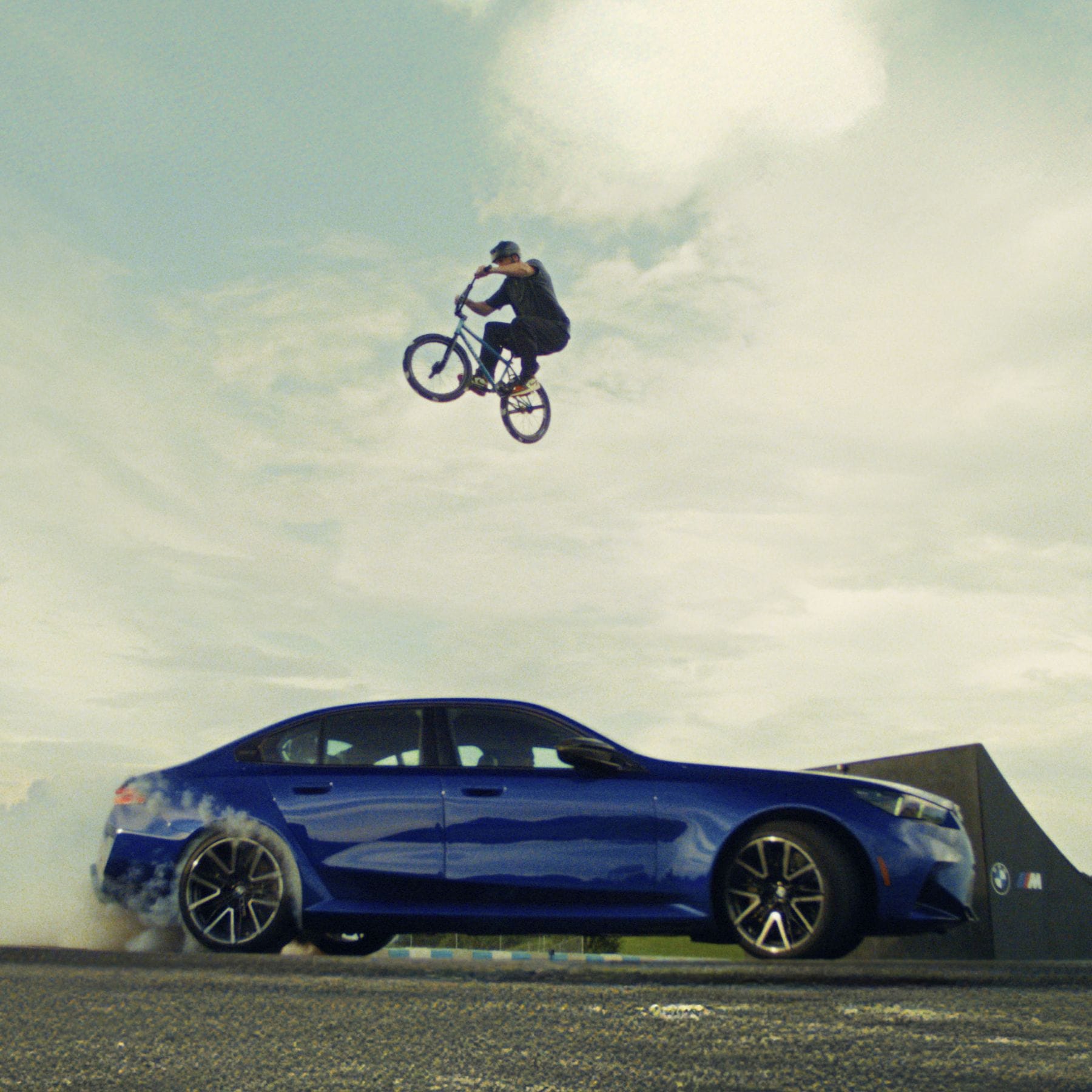 BMX athlete Billy Perry jumps over a drifting BMW M5 Sedan