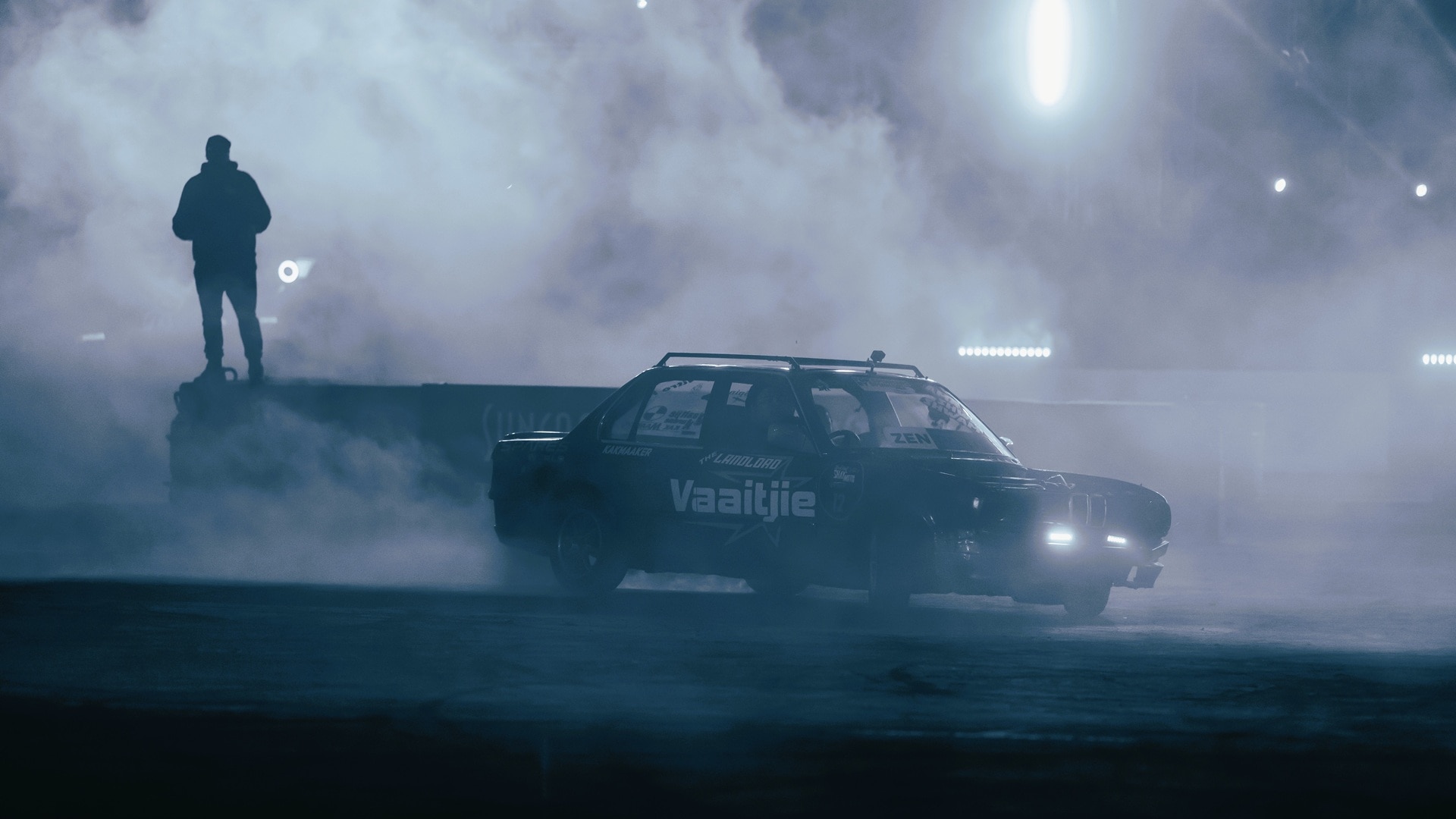 Vic Pardal moderiert ein Spinning-Event von einem Podest, während ein BMW E12 Spinning-Kunststücke unter ihm ausführt.