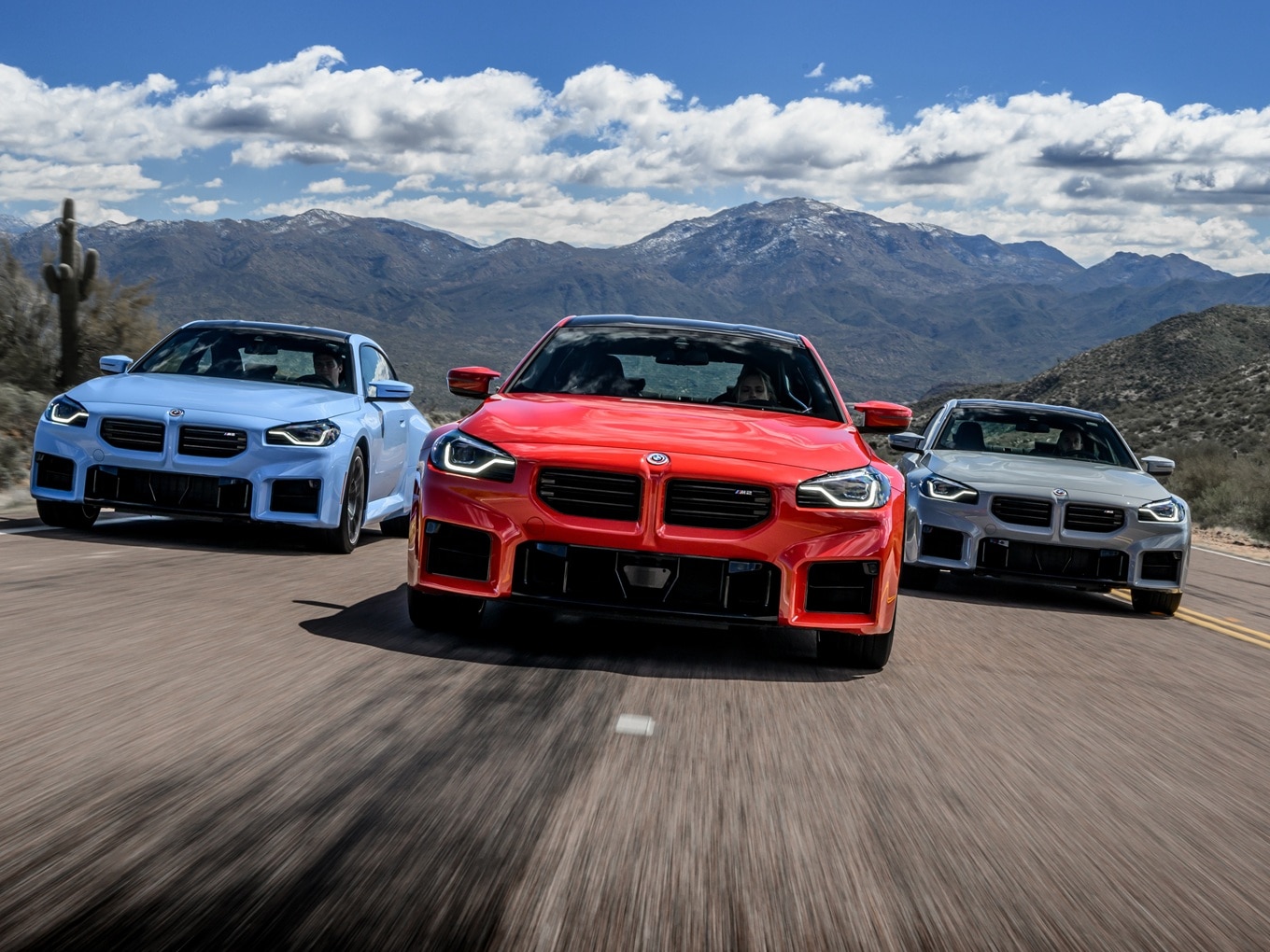 Three BMW M2 G87 in colours Zandvoort Blue, Toronto Red and Brooklyn Grey driving side-by-side on an interstate in the USA. 