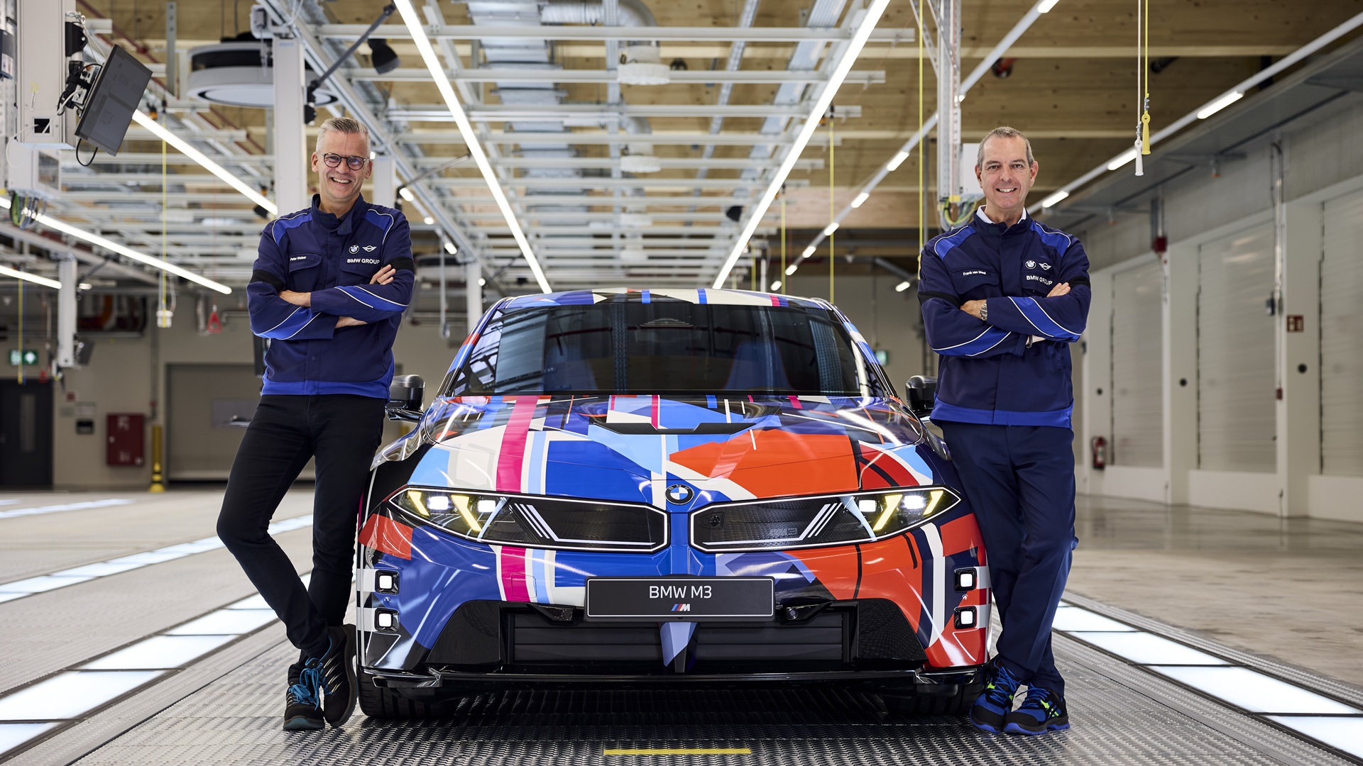 Peter Weber und Franciscus van Meel stehen an einem Vorserienmodell des vollelektrischen BMW M3.
