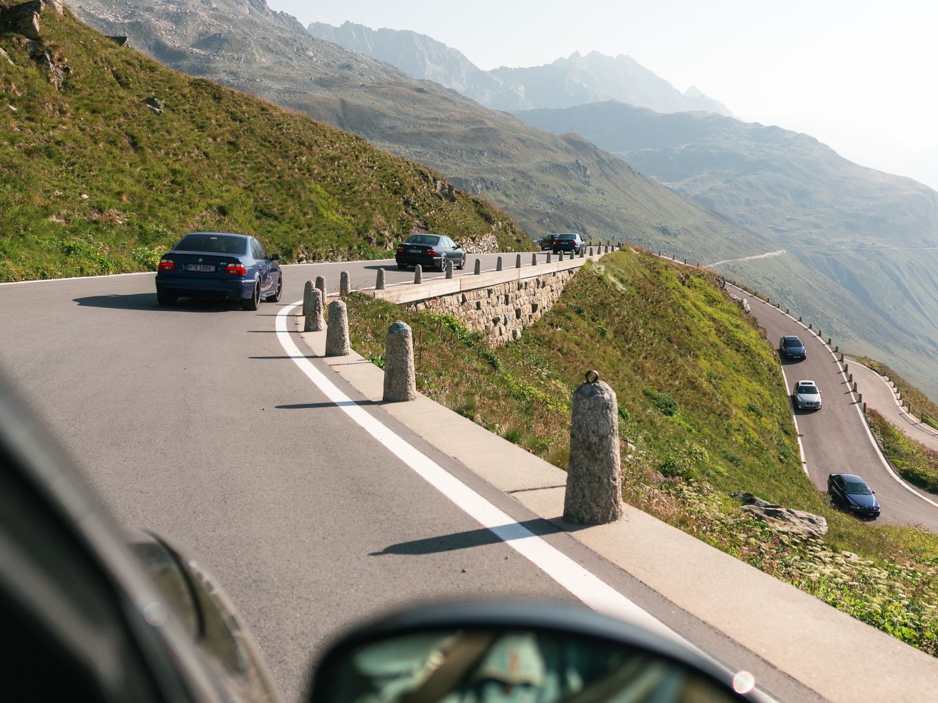 Eine Reihe älterer BMW M5 Modelle fährt auf einer Gebirgsstraße. 