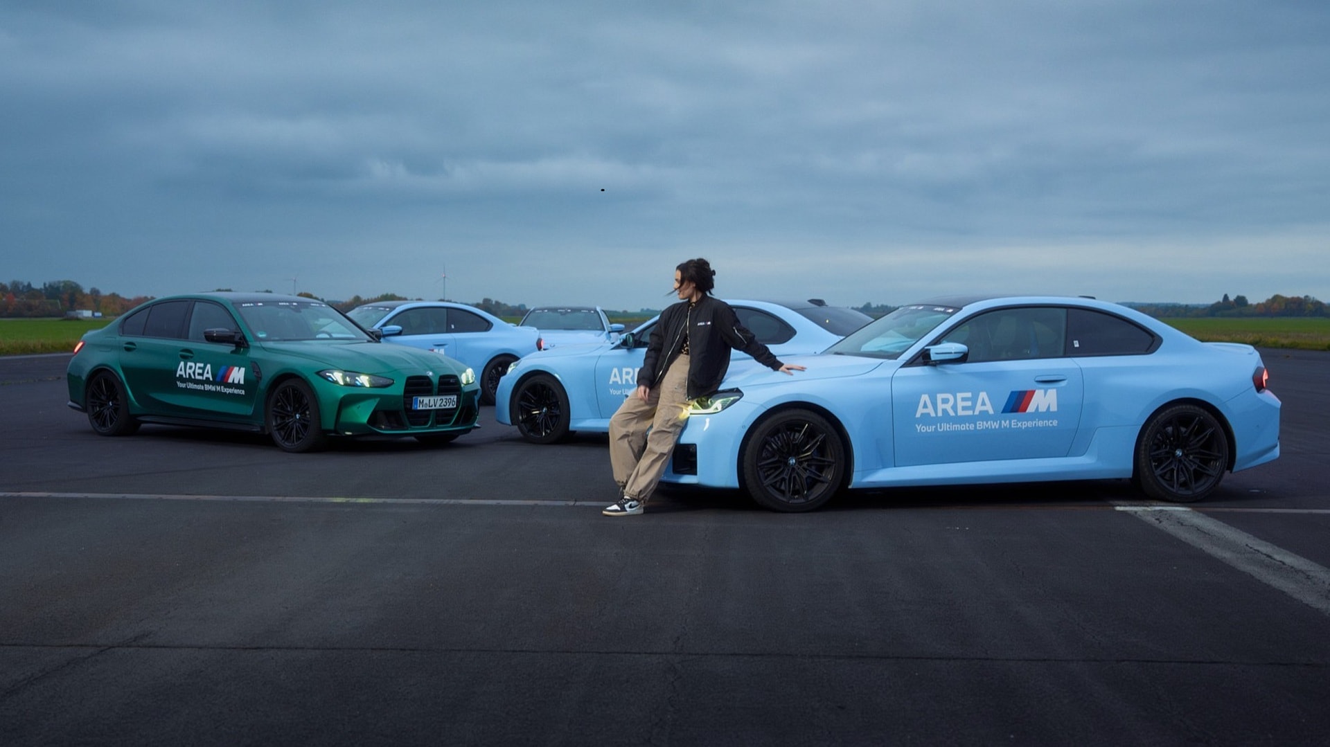 Becky Evans at AREA M site at Maisach, leaning against a BMW M2.