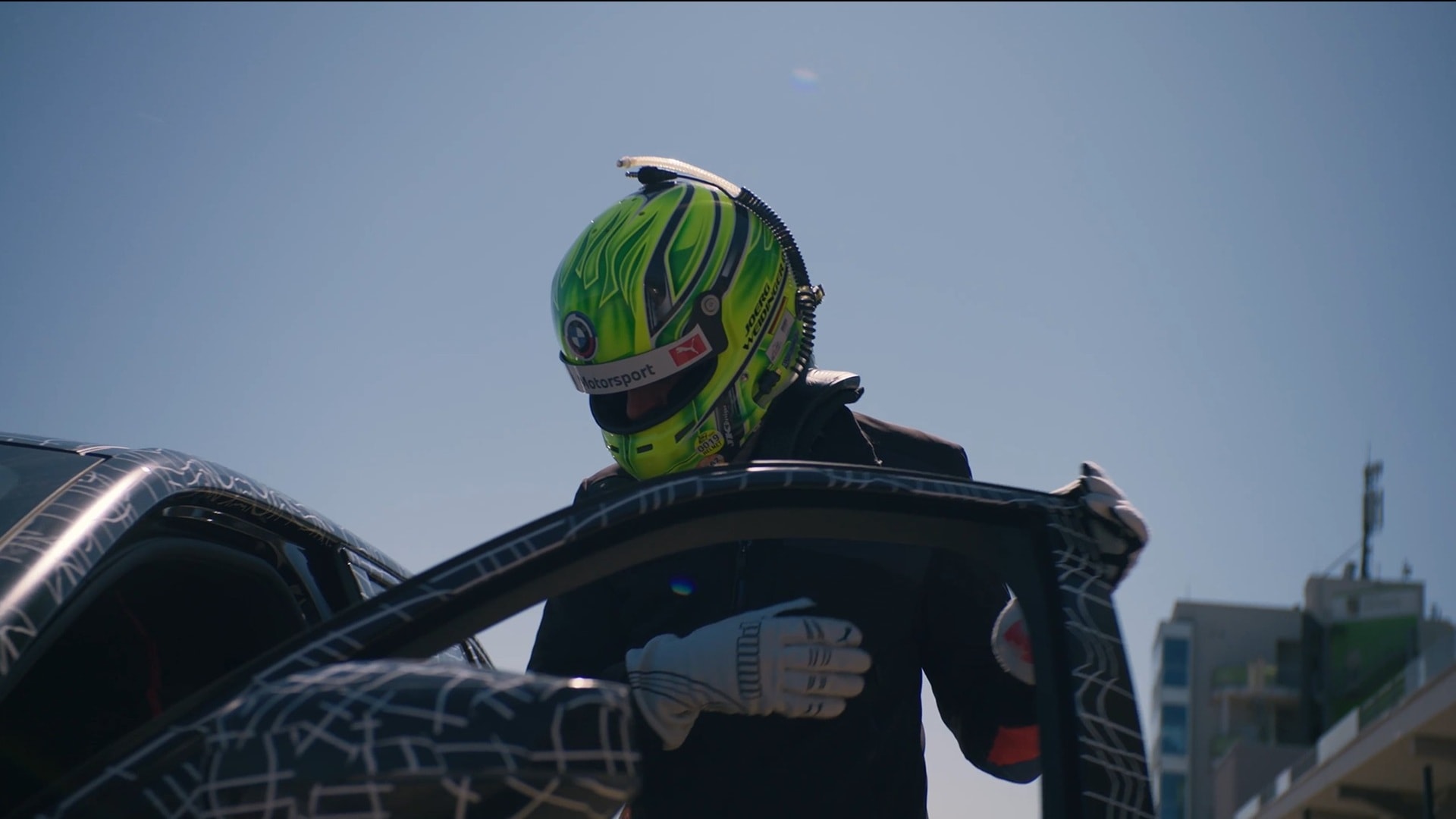 Racing driver Jörg Weidinger, geared up with overall and safety helmet, enters a test vehicle.