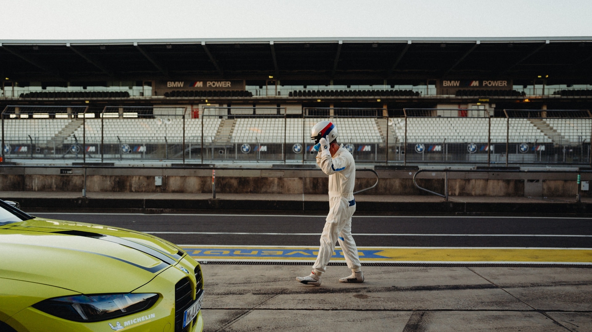 A race car driver in the pit lane of a racetrack, putting on his safety helmet 